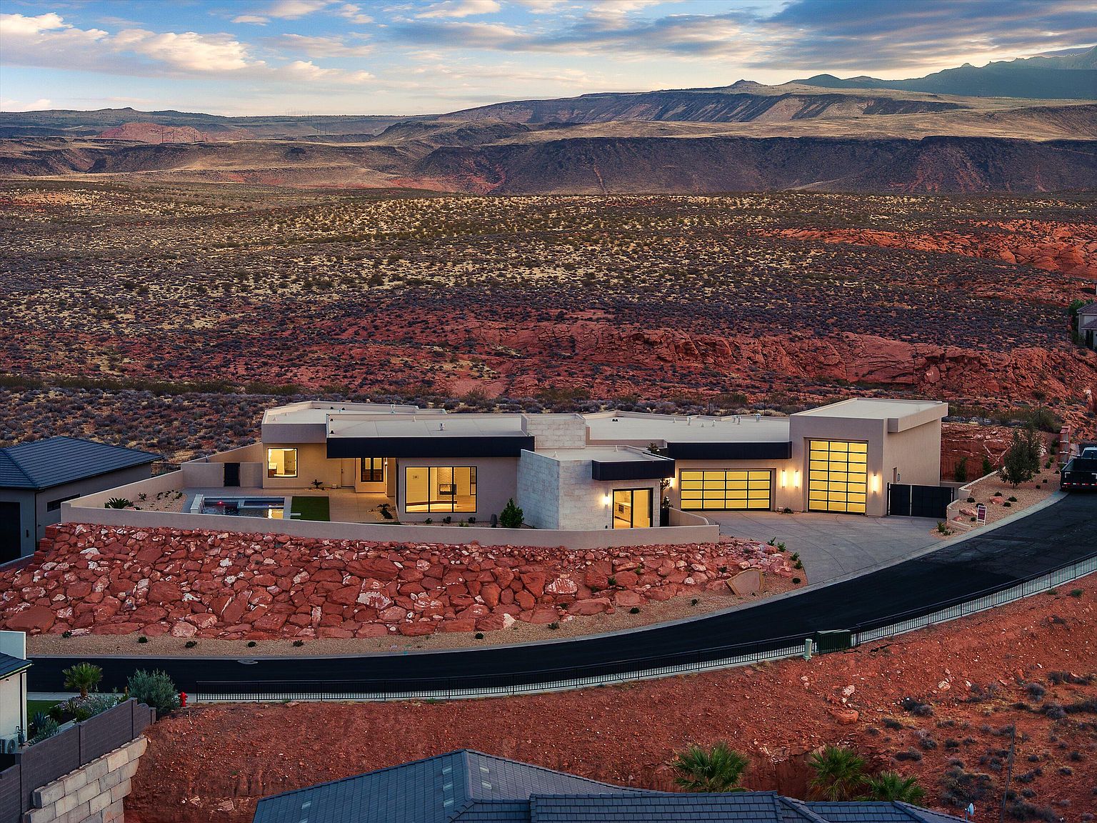 Aerial twilight view of 147 N Westgate Hills Drive set into a red sandstone hillside with desert valley views opening south behind the home